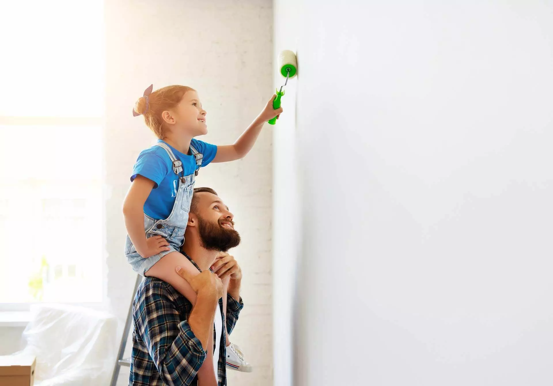 Ein Vater trägt seine Tochter auf seinen Schultern währen sie eine Wand streicht.